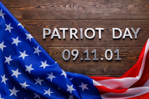 words patriot day laid with silver metal letters on wooden board surface with crumpled usa flag