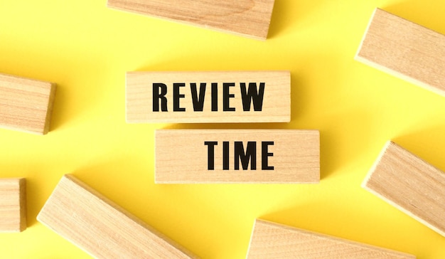 The words REVIEW TIME is written on a wooden blocks on a yellow background