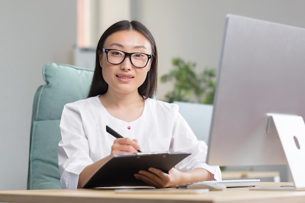 The work of a doctor young beautiful asian woman doctor in glasses and medical gown in the office