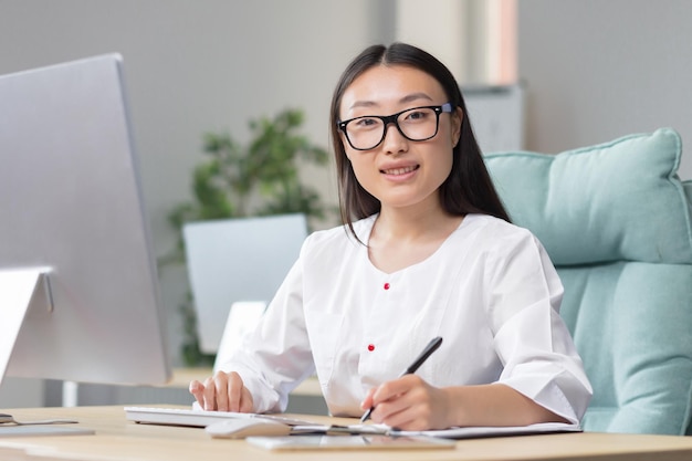 The work of a doctor young beautiful asian woman doctor in glasses and medical gown in the office