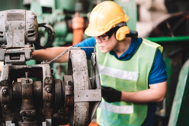 Work at factory.Asian worker man  working in safety work wear with yellow helmet using machine.in factory workshop industry meeting professional