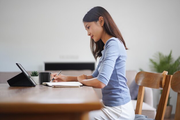 Work from home concept Business women reads financial data on tablet and taking notes in notebook