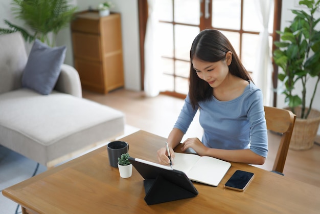 Work from home concept Business women taking notes while reads data on tablet in living room