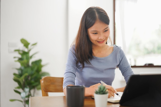 Work from home concept Business women taking notes while reads data on tablet in living room