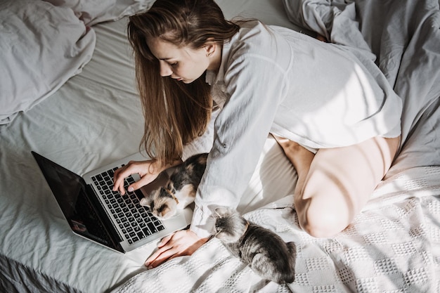 Work from home remote online work home office woman working on laptop in bed and playing with cute