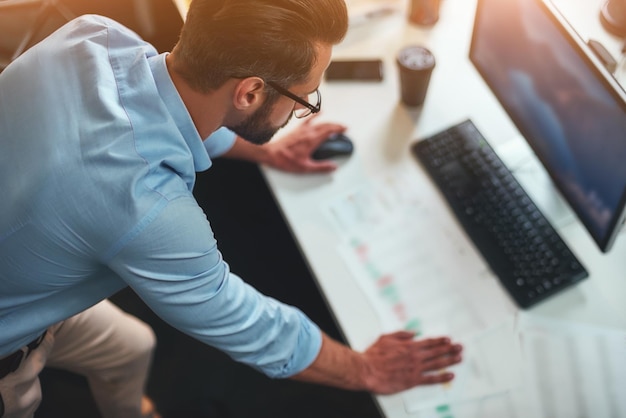 Photo work hard young bearded businessman in eyeglasses and formal wear using computer while standing in the modern office