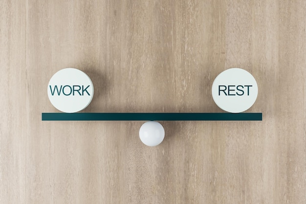 Work life balance concept with scales from board on a ball and equal weight plates with words work and rest on wooden background