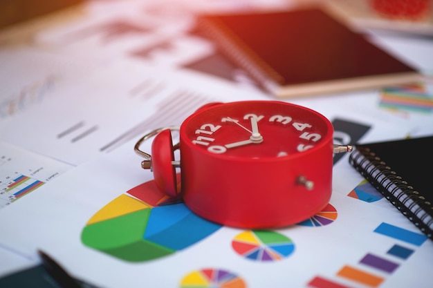 Work planner with red clock time on desk with business chart graph