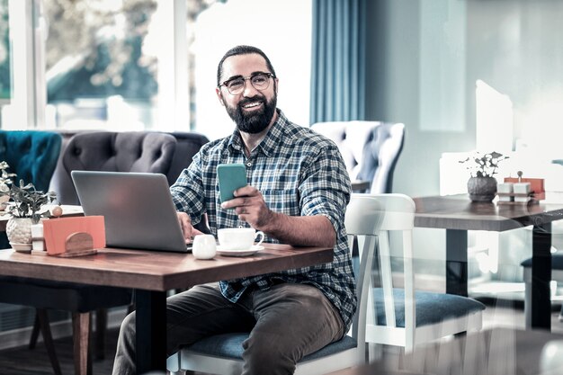 Work remotely. Successful businessman wearing squared shirt working remotely sitting in restaurant