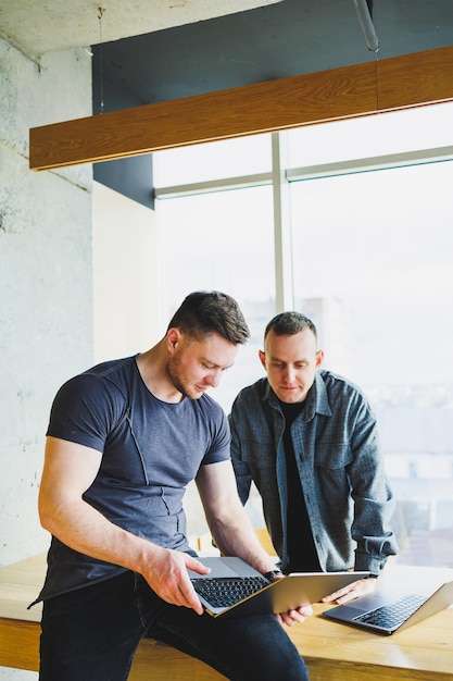 Photo work of two colleagues sitting together while exchanging ideas with a laptop in a meeting room and analyzing work charts work in a modern spacious office