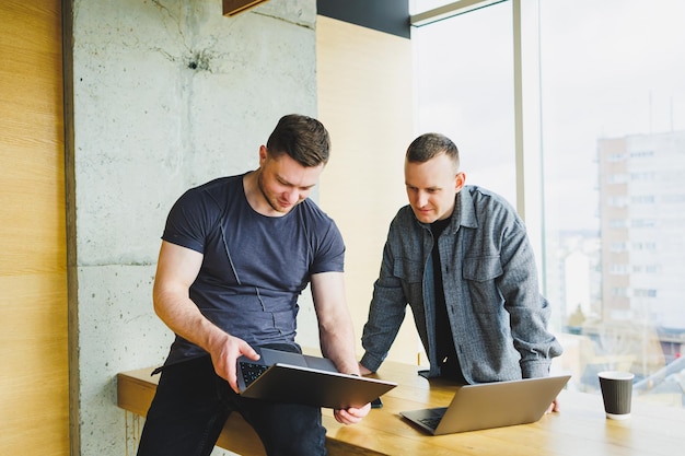 Photo work of two colleagues sitting together while exchanging ideas with a laptop in a meeting room and analyzing work charts work in a modern spacious office