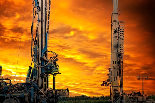 The work of two drilling rigs at a construction site against the backdrop of sunset Exploration of useful minerals Industry and construction