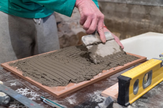 Worker applies cement adhesive on the tiles. Finishing works. The technology of laying tile