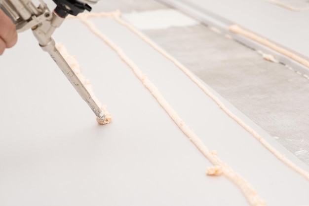 Worker applying foam with glue gun on sheet of styrofoam for gluing it to the floor in house