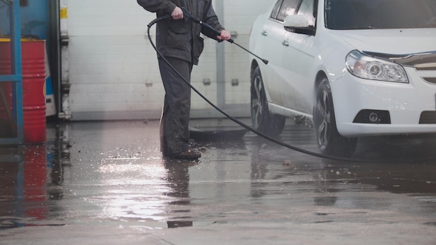 Worker in auto service is washing a car in the suds by water hoses telephoto