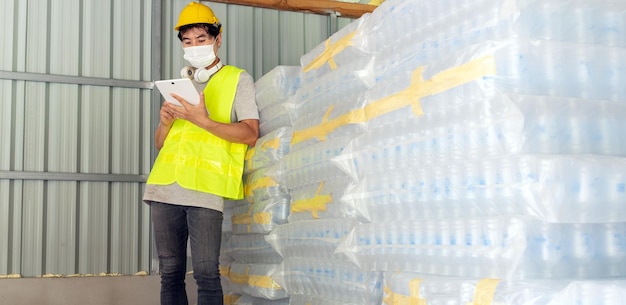 worker checking the stock of plastic bottles in the warehouse using a tablet to update online stock