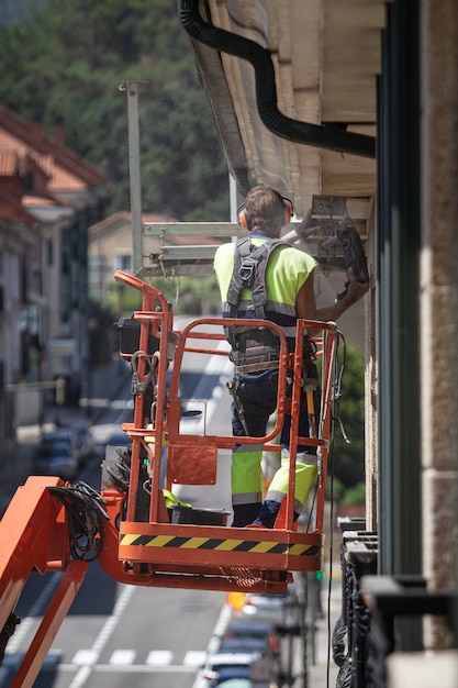 Worker on a crane with a drill working at height in a building ledge