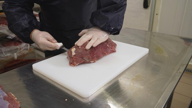 Photo worker cuts raw meat with sharp knife into steaks