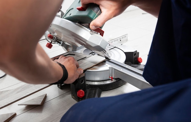 A worker cuts a skirting board made of fibreboard with a miter saw