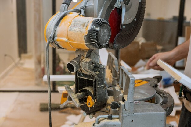 Worker cuts the wood moldings baseboard on the miter saw