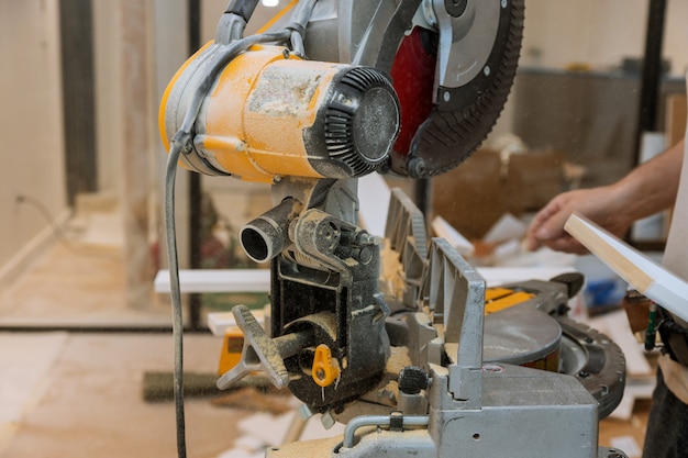 Worker cuts the wood moldings baseboard on the miter saw