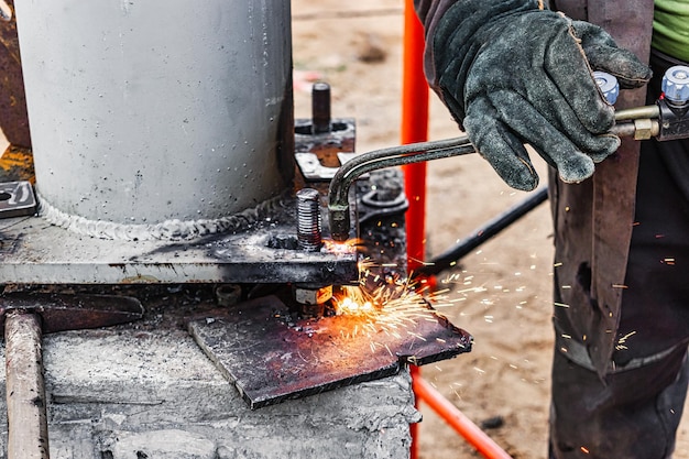 Worker cutting metal plate by Gas Cutting Torch at a construction site Installation of a metal structure Closeup The welder performs the installation of metal structures Sparks from welding