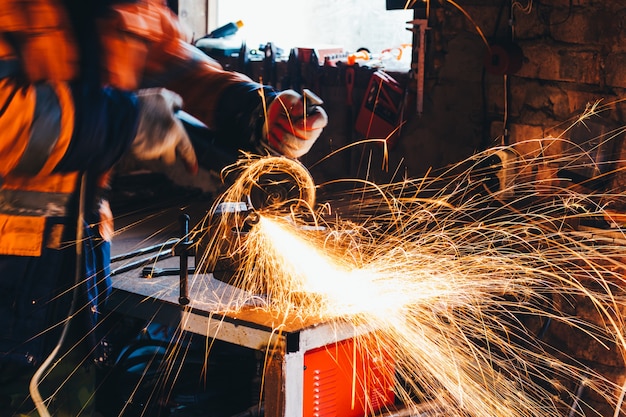 Worker cutting metal with grinder in his workshop. Sparks while grinding iron.