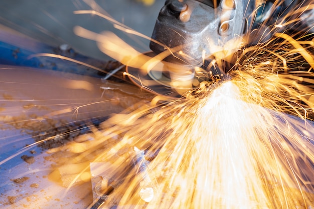 Worker cutting steel with grinding machine and splashes of sparks in workshop