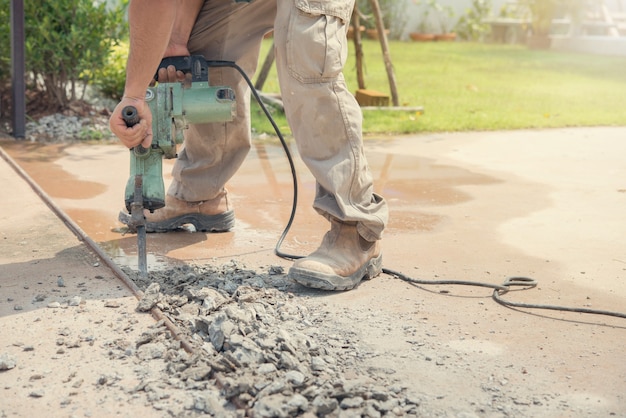  Worker drilling concrete driveway with jackhammer.