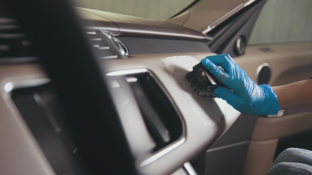 Worker female in gloves is washing with brush a car interior, close up view