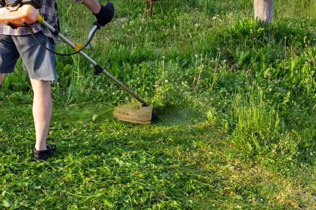 The worker of a garden cuts off a grass. The man in a uniform of the general worker works at a lawn. Work of municipal services on improvement of territories.