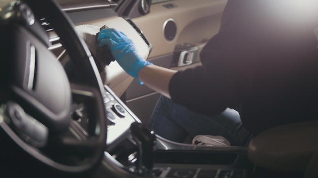 Worker in gloves is washing with brush a car interior and seats, close up