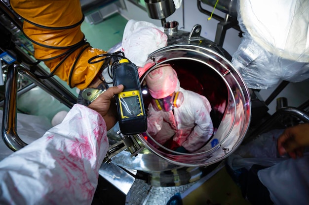 Worker hand holding gas detector inspection safety gas testing at front manhole stainless tank to inside confined