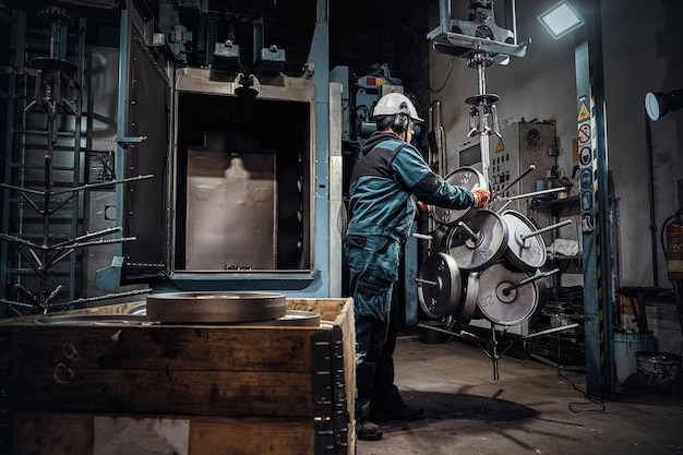 Worker in helmet is putting freshly made metal weight to the storage at metal factory.