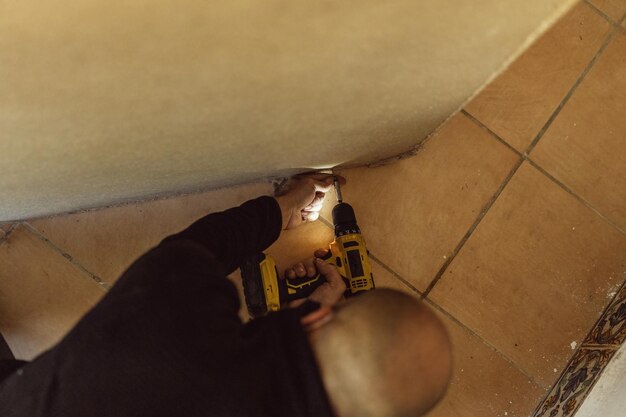 Worker on his knees unscrewing with an electric screwdriver the screws of a piece of furniture in a moving operation