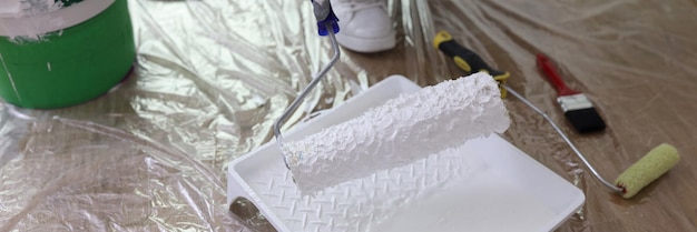 Worker holds roller brush over tray in renovated room closeup builder ready to apply white