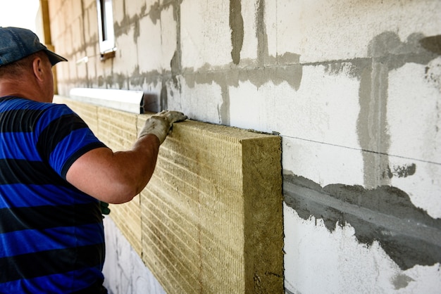 Worker insulates the house with mineral wool slabs. Internal thermal insulation of walls with mineral wool.