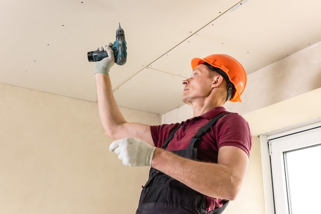 Worker is using screws and a screwdriver to attach plasterboard to the ceiling