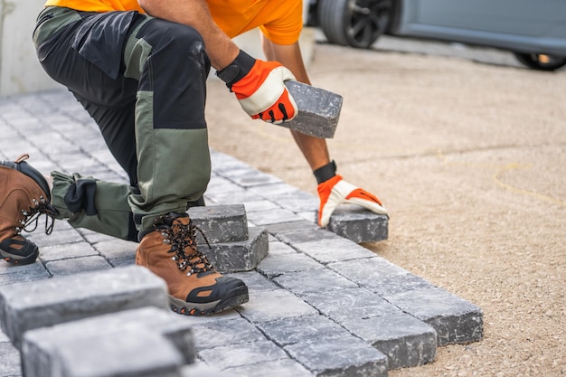 Photo worker laying paving stones on a driveway at a construction site in bright daylight