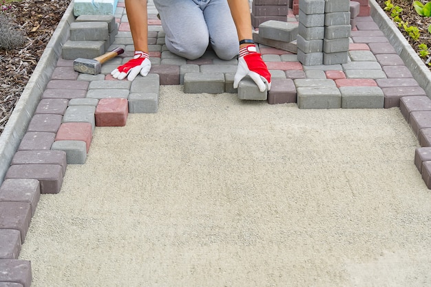 worker laying paving stones. stone pavement, construction worker laying cobblestone rocks on sand.