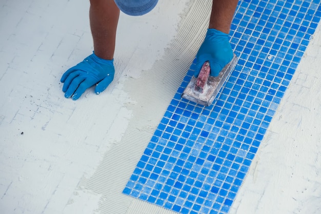 Worker laying tile in the pool. Pool repairing work.