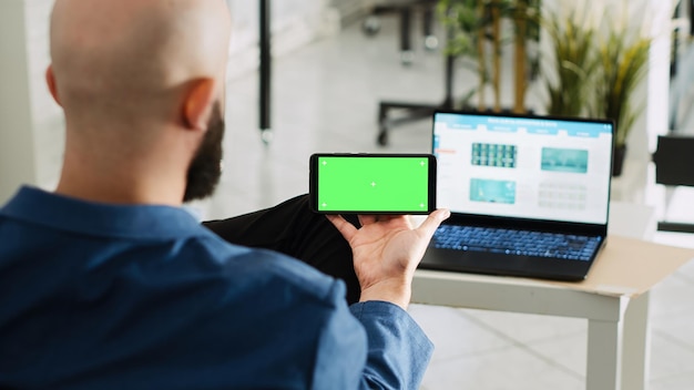 Worker looking at greenscreen display preparing to do research for small business plan Young adult holding smartphone with isolated copyspace mockup open floor office space