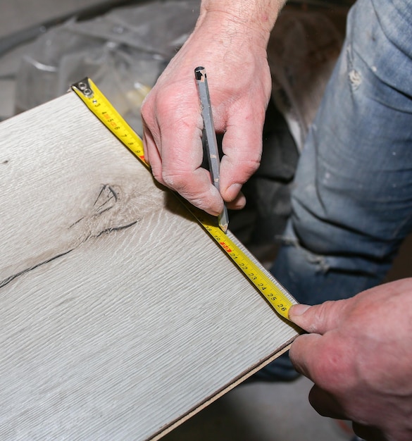 Worker making laminate flooring in apartment Measure tape and pencil in hands Maintenance repair renovation Wooden parquet planks indoors