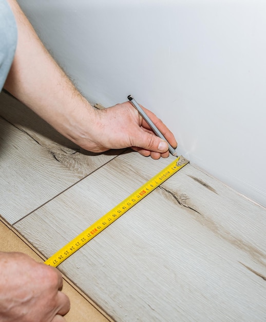 Worker making laminate flooring in apartment Measure tape and pencil in hands Maintenance repair renovation Wooden parquet planks indoors