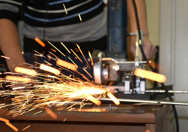 Worker man cutting a metal pipe in two pieces and lot of sparks flying straight into the camera close-up.