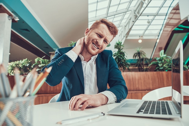 Worker man's neck hurts at desk in office.