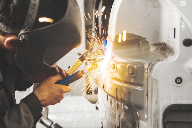 Worker in mask welds car in auto service of bodywork Industrial concept of vehicle repair