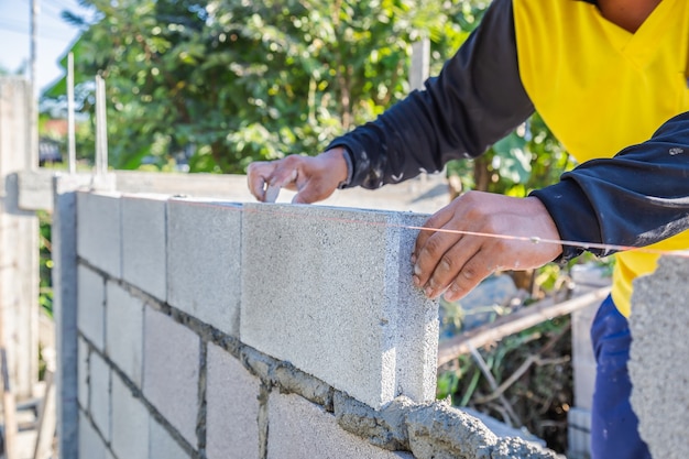 Worker masonry are building walls with cement blocks and mortar by building up in layers.