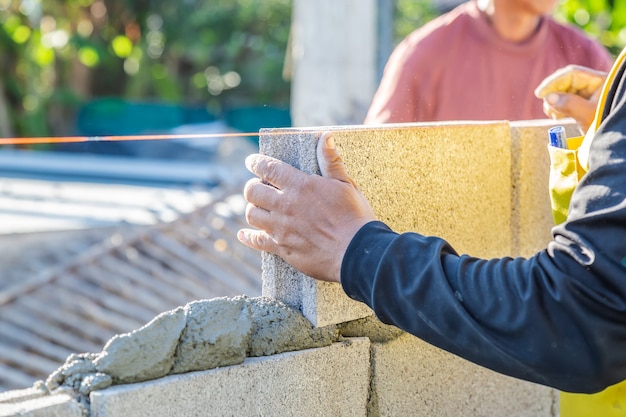 Worker masonry are building walls with cement blocks and mortar by building up in layers.