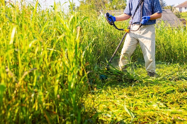 A worker mows tall grass with an electric trimmer